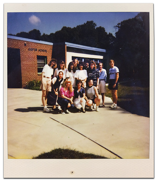 Color Polaroid photograph of North Springfield Center staff taken during the 1993 to 1994 school year. 13 adults are standing on the sidewalk in front of the building. Lettering on the wall near the entryway reads: Center School. 